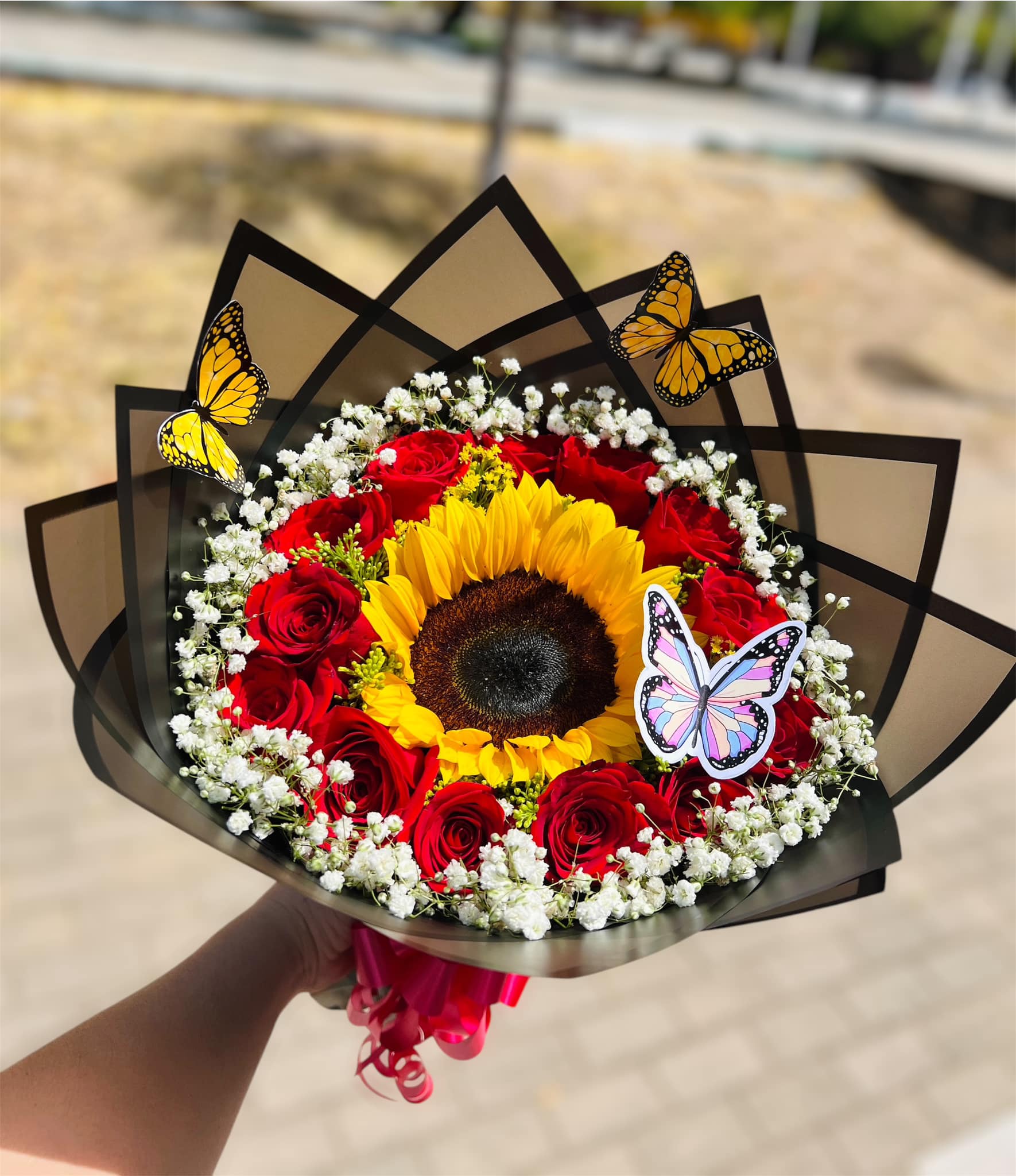 Ramo de girasol con rosas rojas, gypsophila y mariposas en papel negro